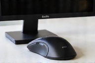 Ergonomic mouse being used on a desk with a monitor in the background